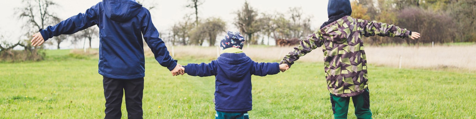 Photo of 3 children from behind holding hands standing in a field