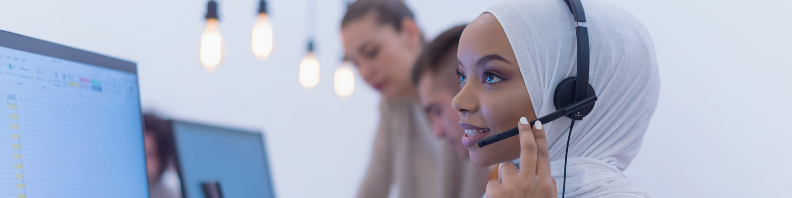 Photo of a woman sat down in front of a laptop wearing a headset and having a telephone conversation.