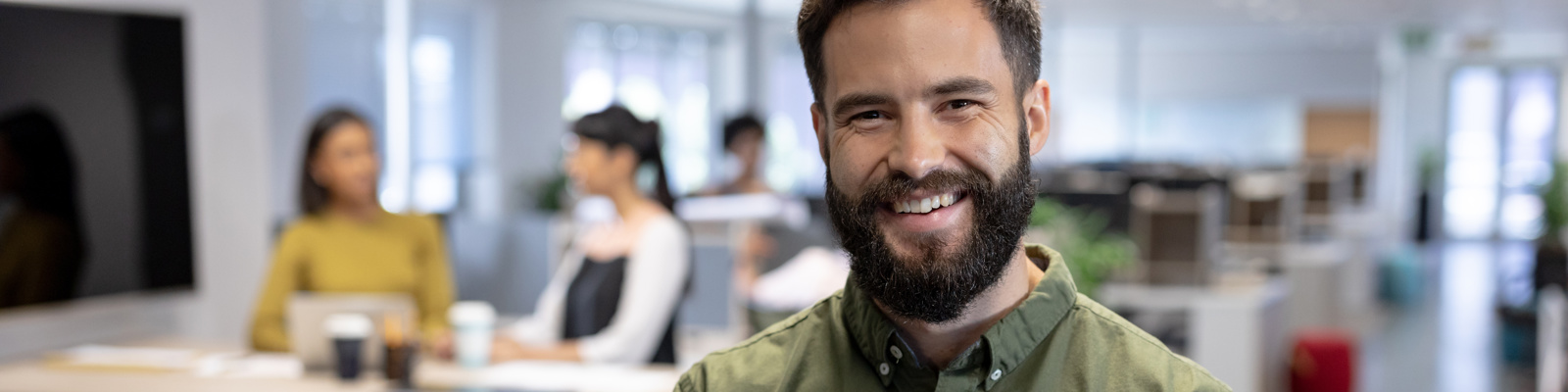 Friendly fundraiser in an olive green shirt holding a tablet and smiling in a modern office break area.