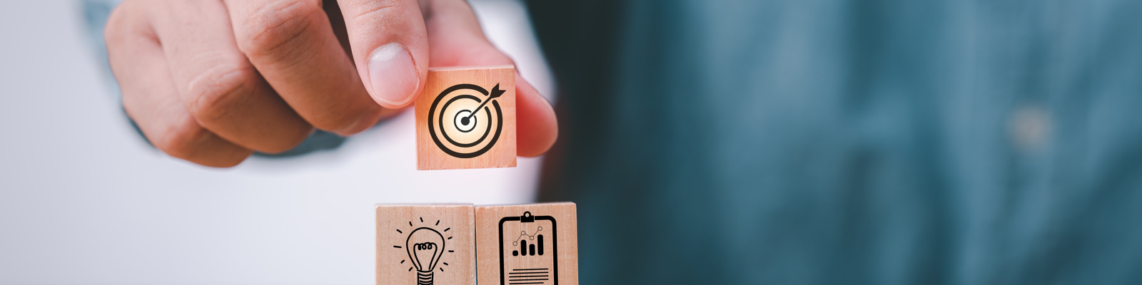 Photo of a hand stacking wood blocks on table with icons that represent a business strategy and action plan.