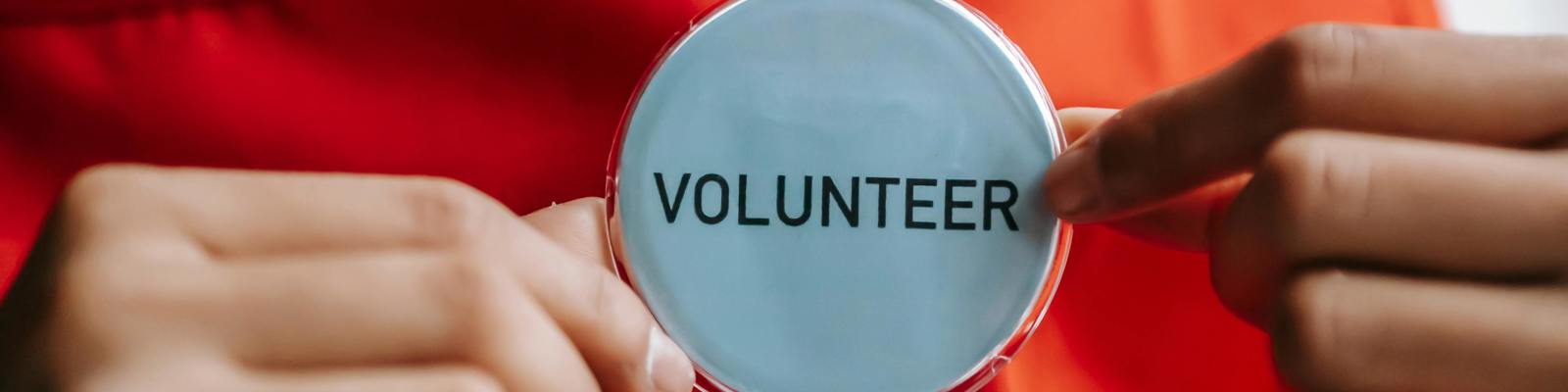 A woman in a red top holds a pin badge which has the word volunteer printed on it